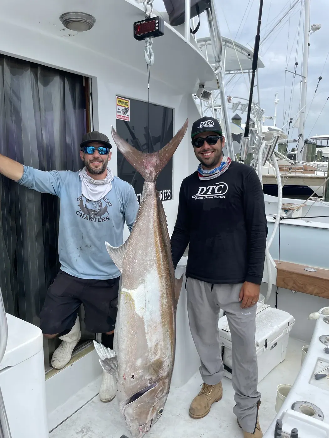Two Double Threat crew members with the boat record 107lb amberjack at the dock in Miami