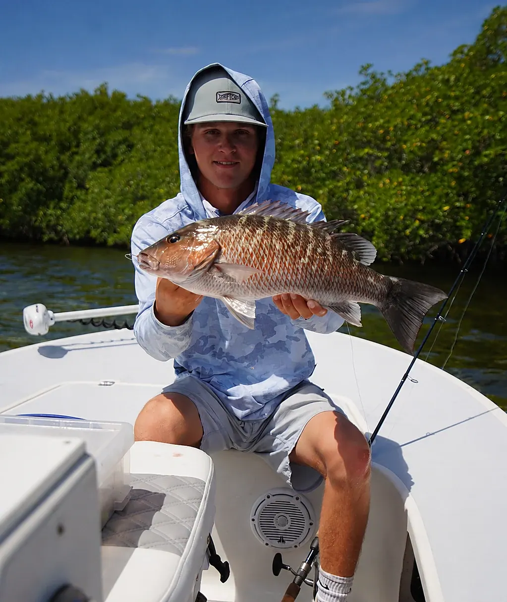 A young angler on the bow holding a mangrove snapper caught inshore off Miami