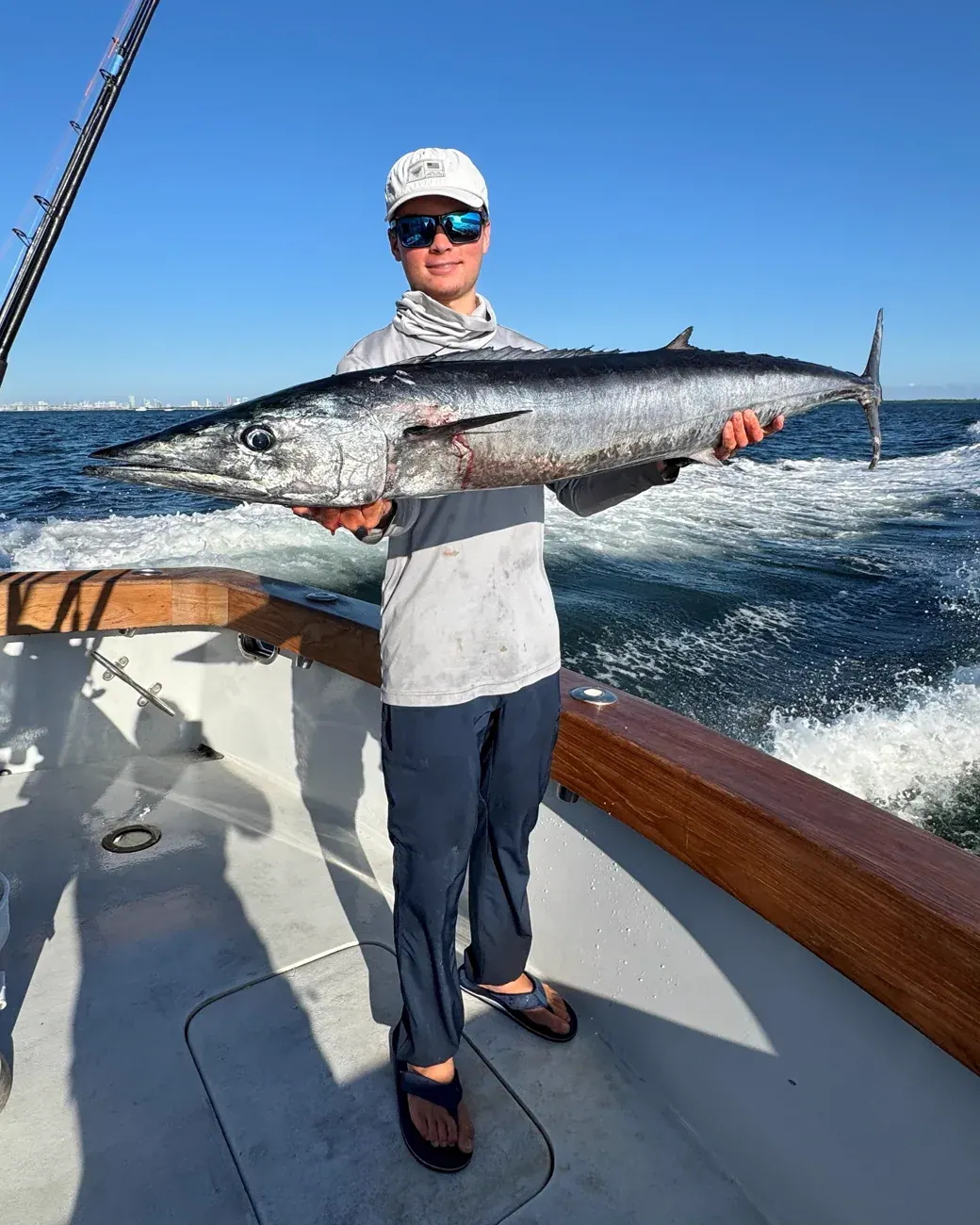 An angler holding a wahoo with the Miami skyline in the background